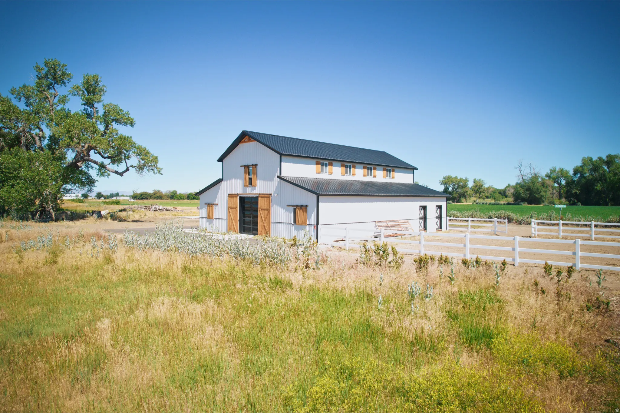 White barn structure featuring a dark roof, exposed wood beam accents, and decorative shutters