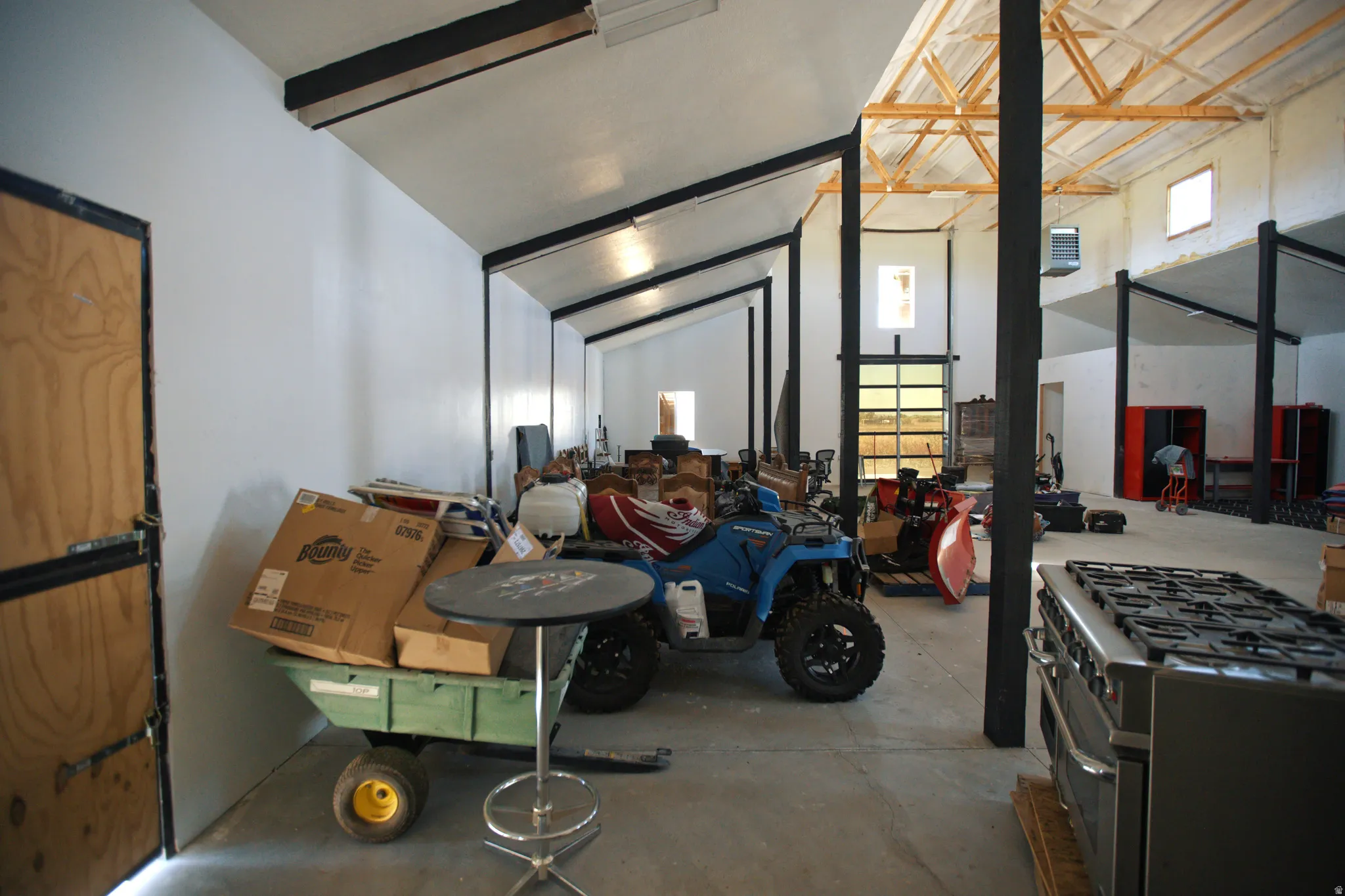 Spacious interior featuring a concrete floor, exposed wooden ceiling beams, multiple skylights, and a roll-up glass garage door