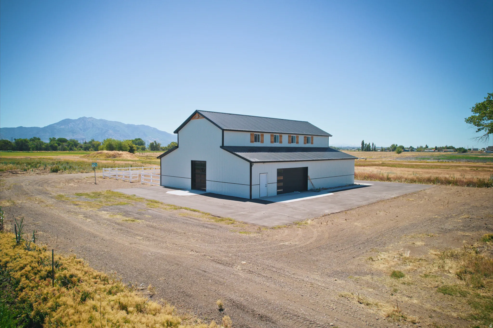White exterior barn structure with a dark metal roof, multiple garage doors, and upper-level windows with wooden shutters