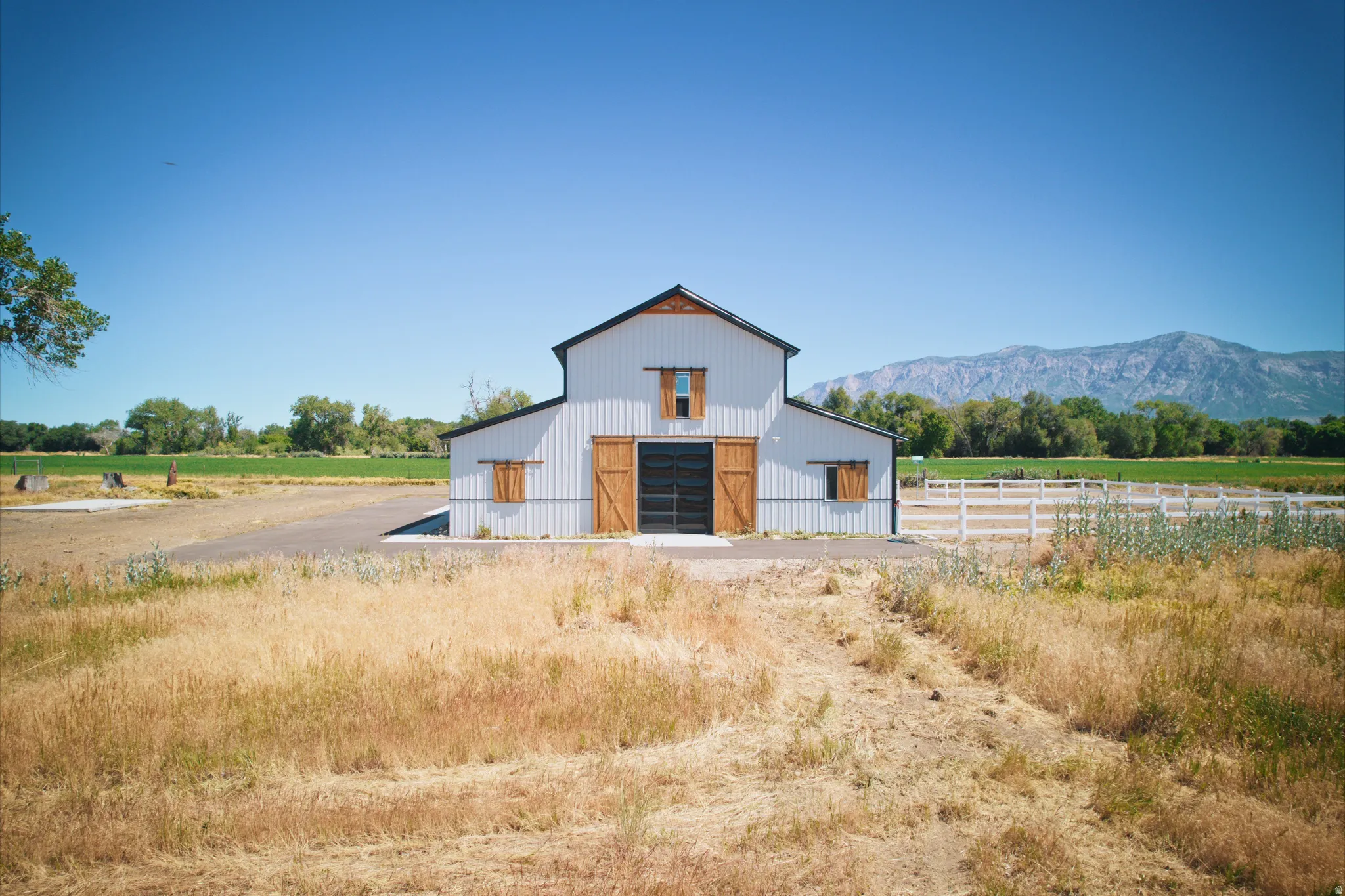 White metal barn with black trim, natural wood doors, and mountain backdrop