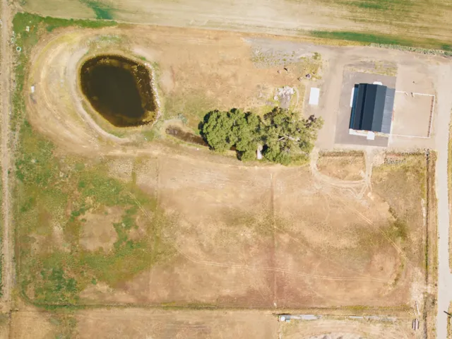Expansive rural property featuring a large barn structure with a dark roof, a natural pond, multiple mature trees, and a network of unpaved access paths across varied terrain