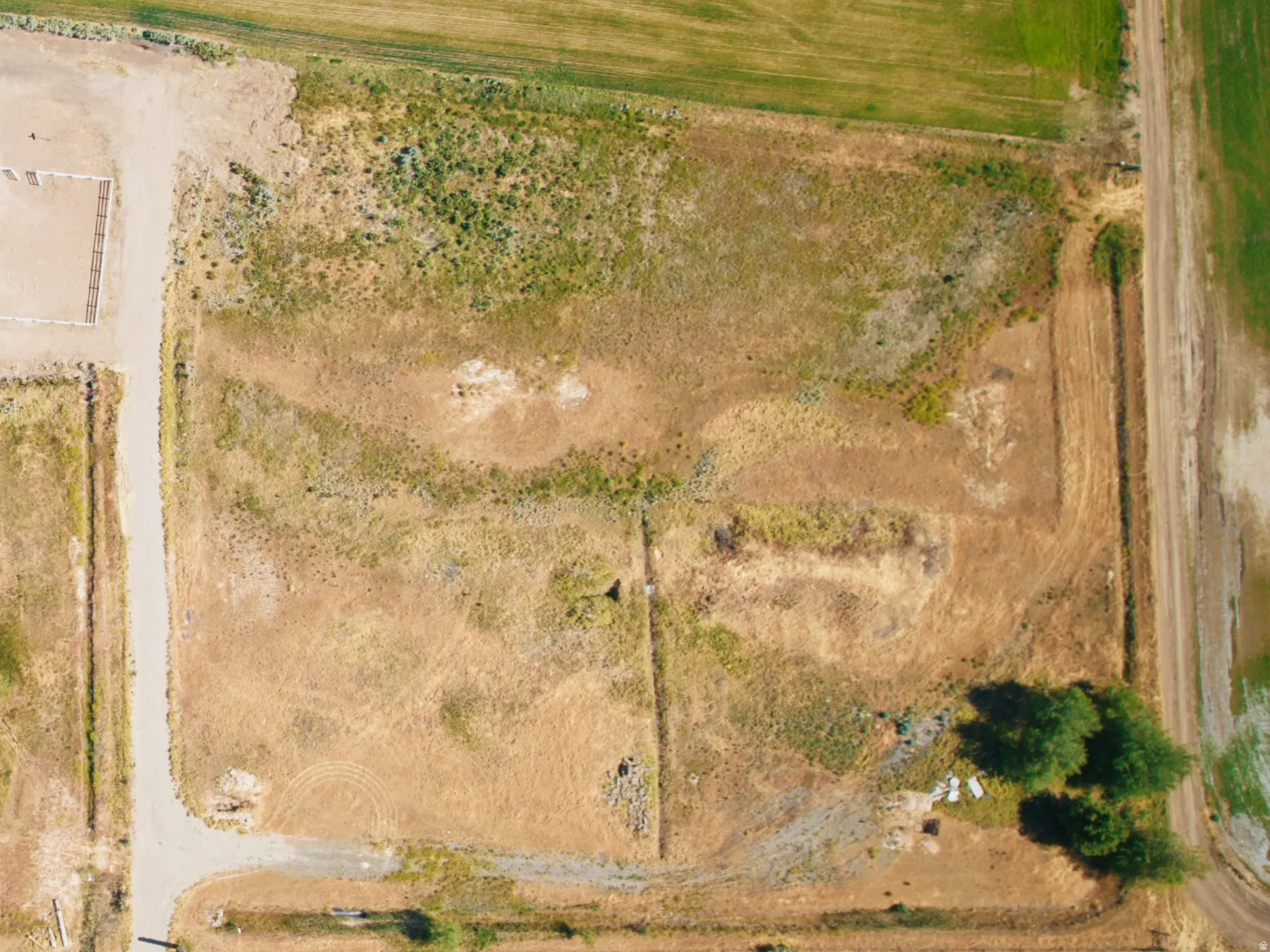 Aerial perspective showcasing expansive acreage with a central rectangular building, a circular pond feature, and a cluster of mature trees