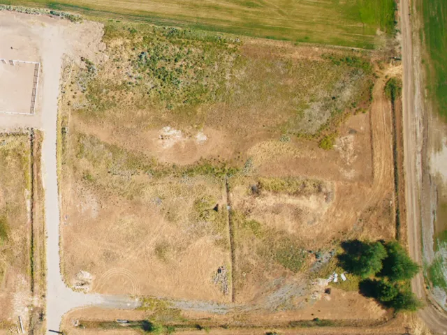 Aerial perspective showcasing expansive acreage with a central rectangular building, a circular pond feature, and a cluster of mature trees