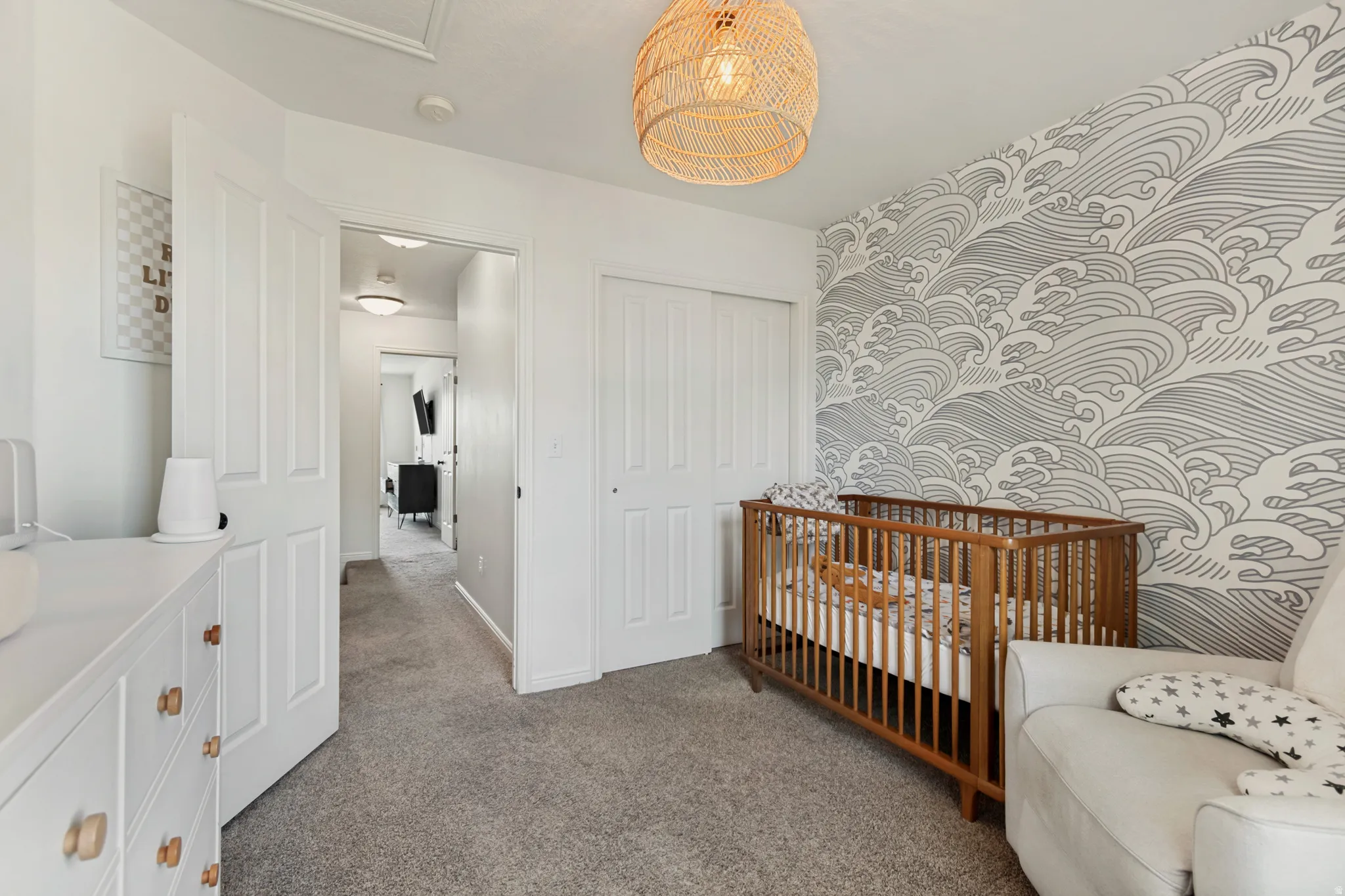 Room featuring a decorative accent wall with a wave pattern, a rattan pendant light fixture, and plush carpet flooring