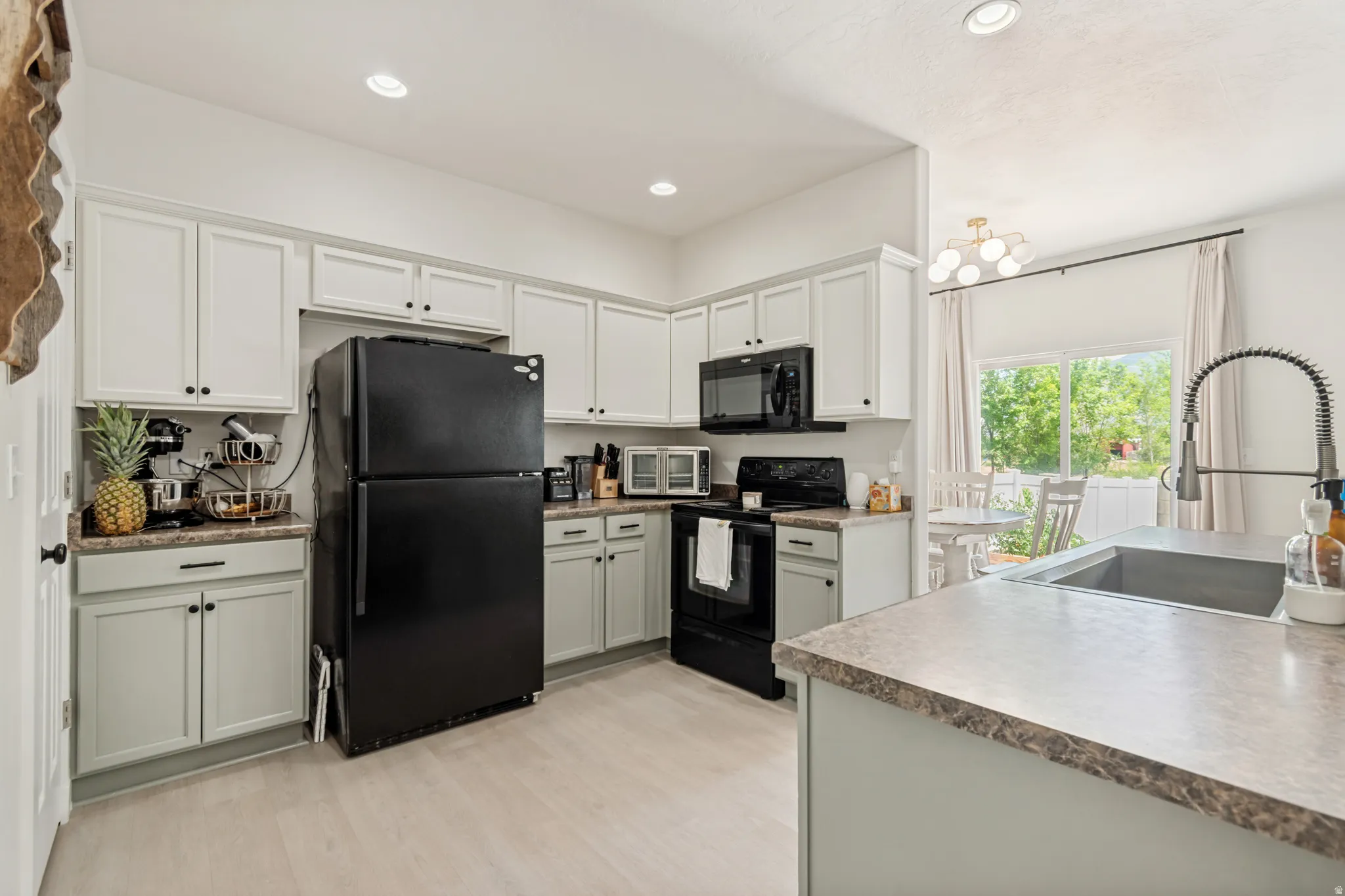 Kitchen featuring light gray upper cabinetry and dark gray lower cabinetry with black hardware, black appliances, laminate countertops, and wood-finish flooring