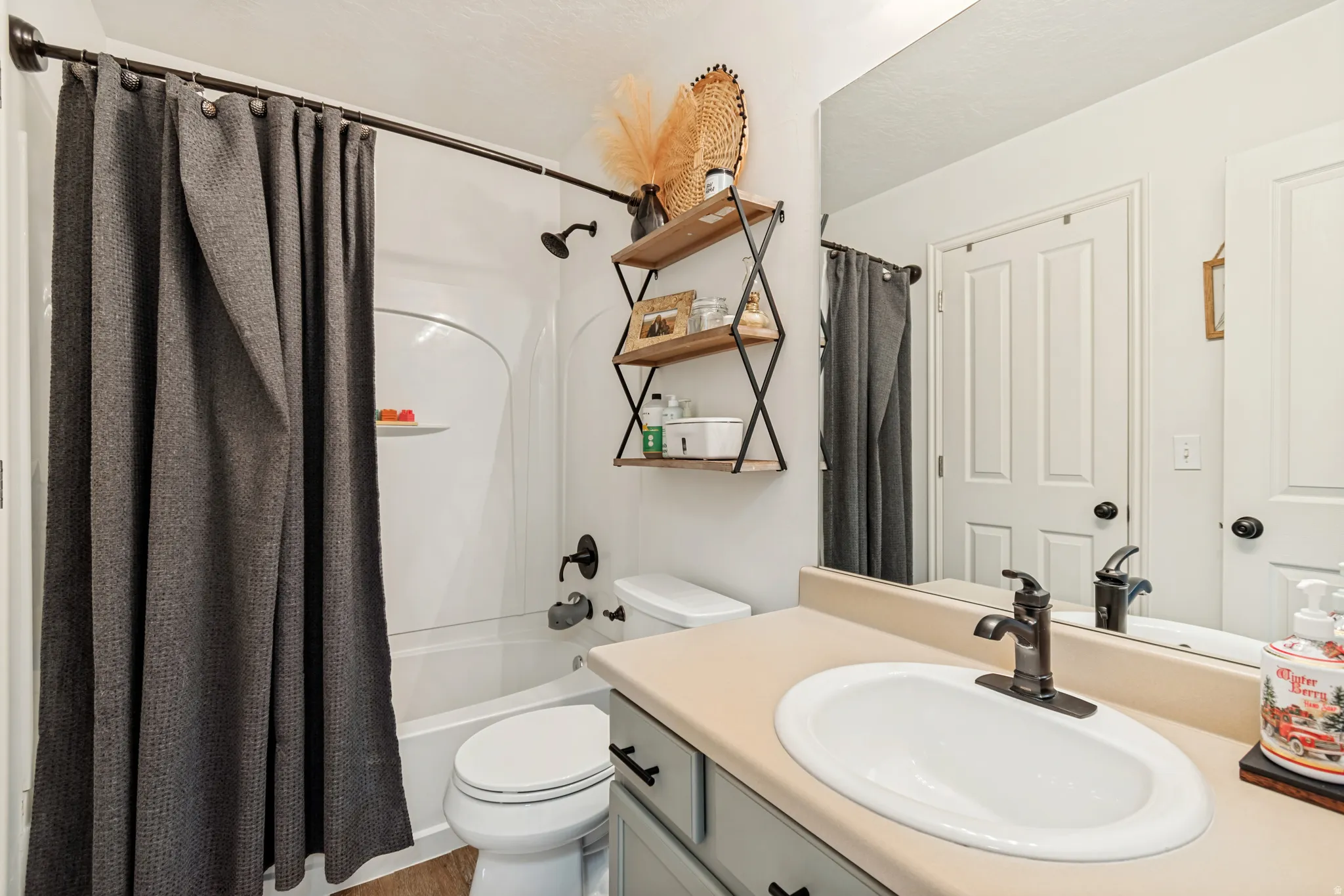 Bathroom featuring a white integrated tub and shower unit, wood-finish flooring, a vanity with an integrated sink, and an expansive mirror