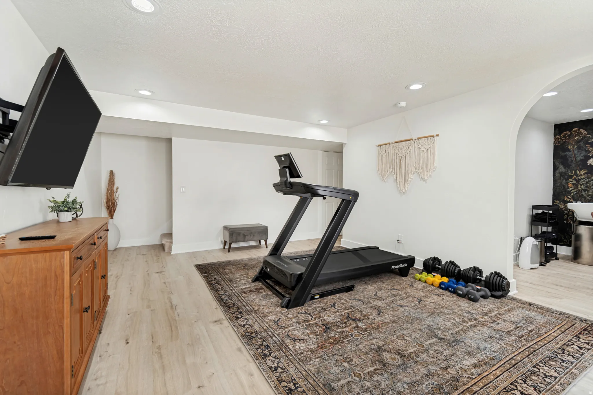 Versatile finished basement space featuring light wood-finish flooring, recessed lighting, and a white color palette