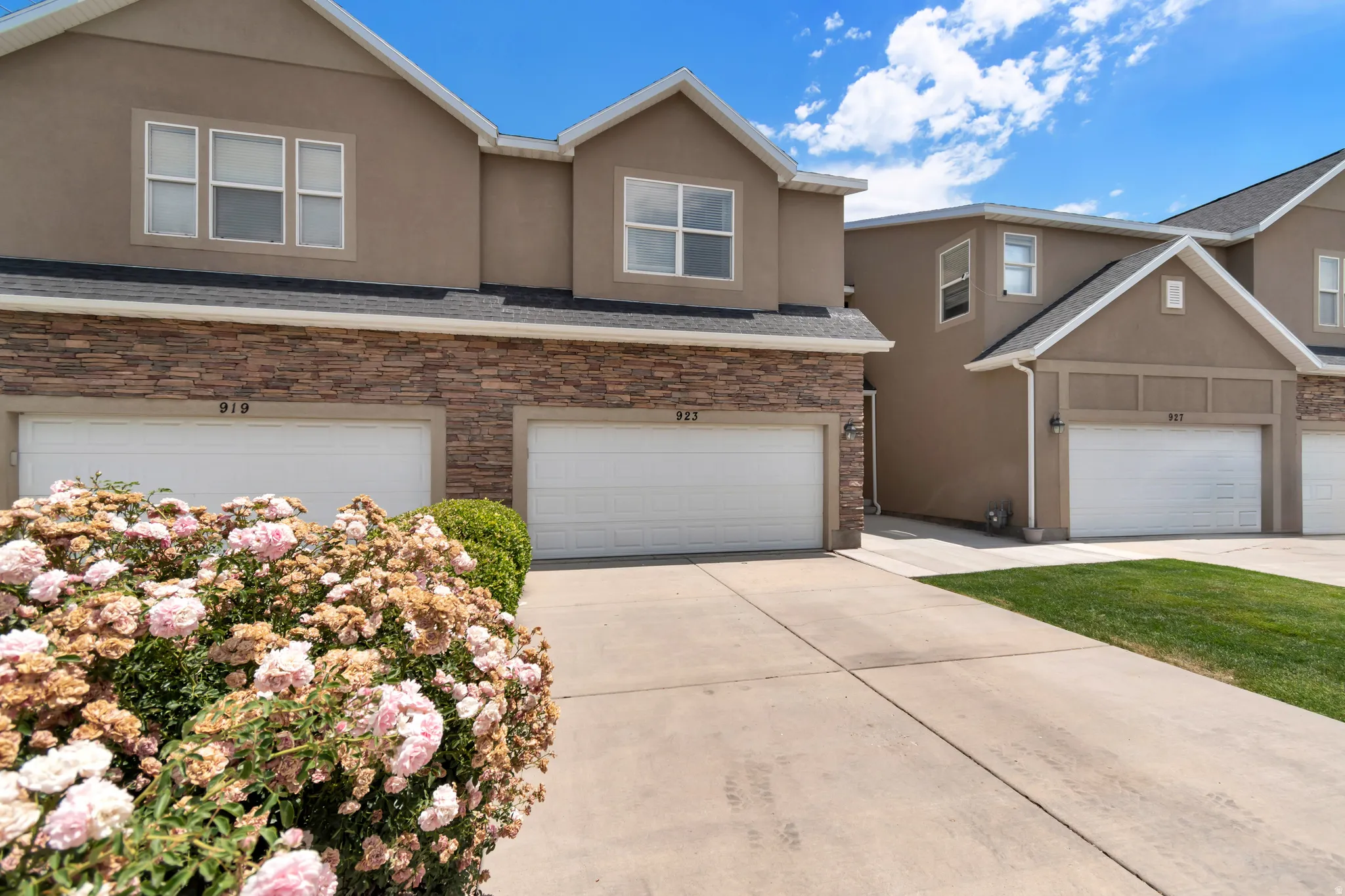 Townhome exterior featuring tan stucco siding, stone veneer accents, individual garage doors, and a concrete driveway