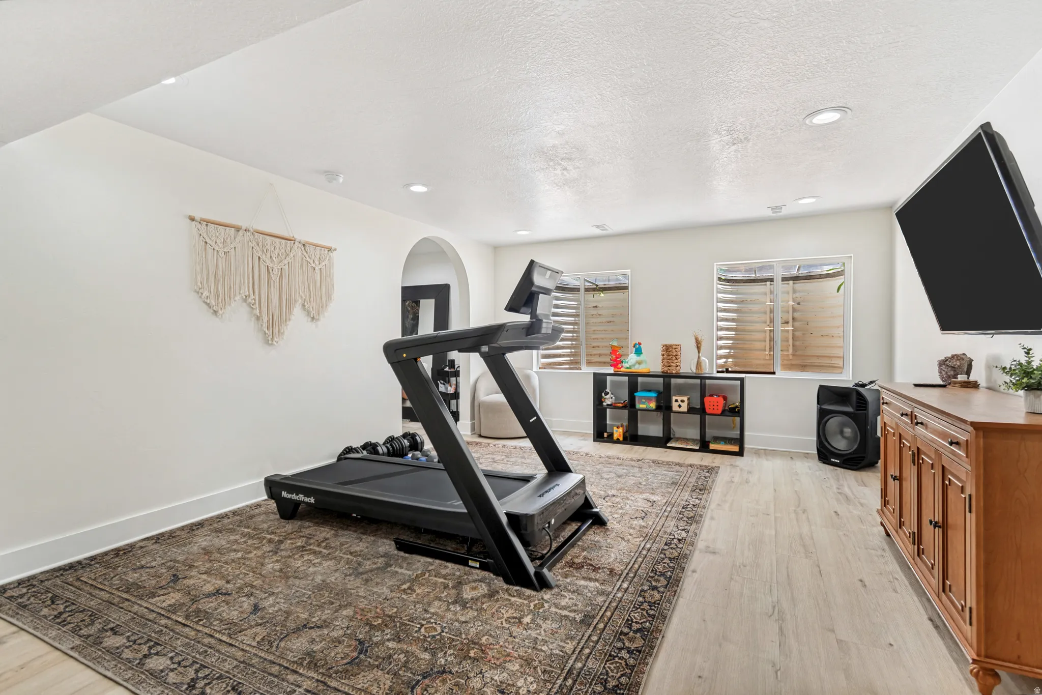 Spacious room featuring light-toned flooring, recessed lighting, and an arched doorway