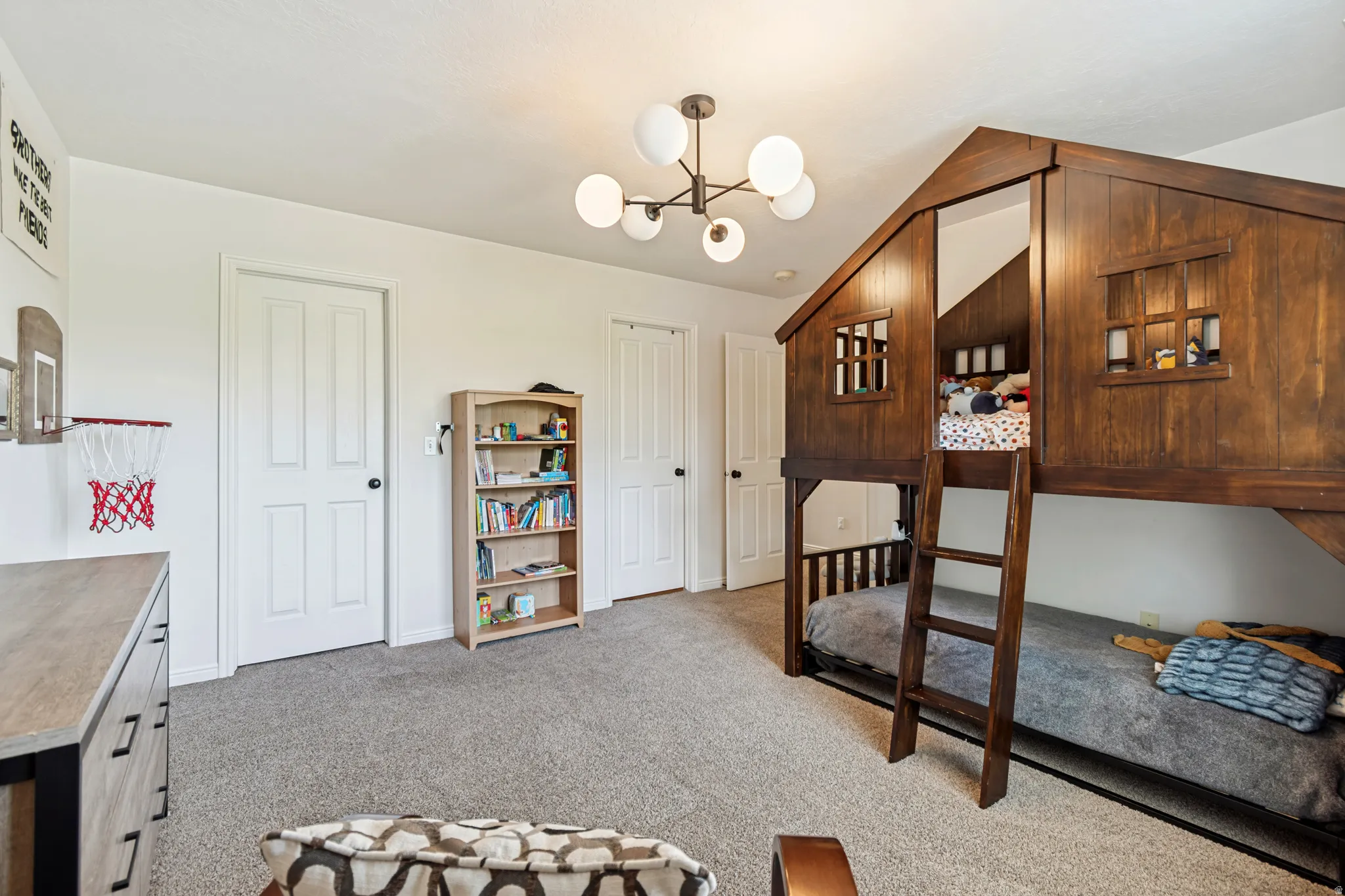 Room featuring a built-in wood-finish bunk bed with an integrated ladder, a contemporary chandelier with spherical globes, light gray carpet, and white trim