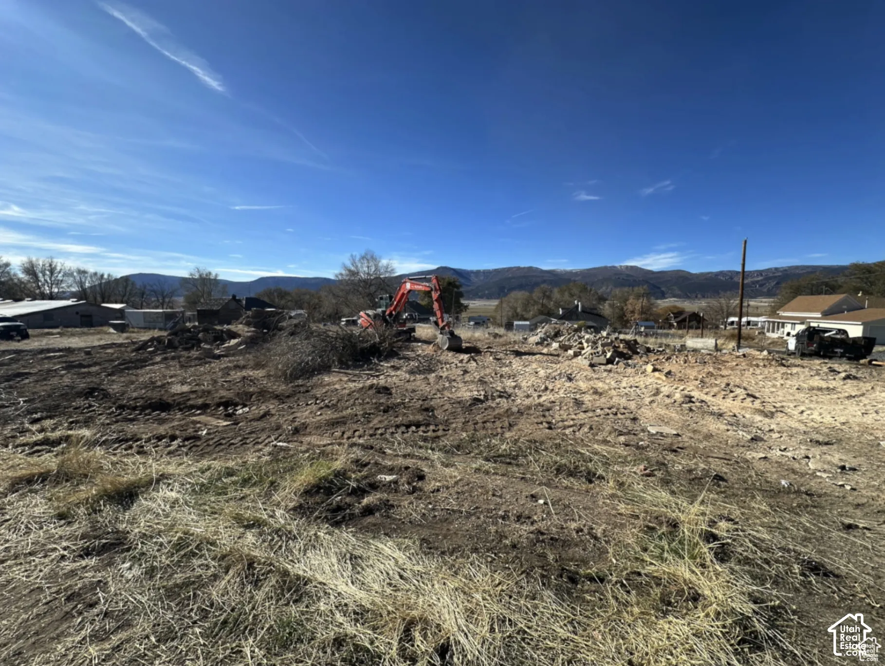 Expansive cleared land parcel with scattered debris, featuring distant mountain ranges and a clear blue sky