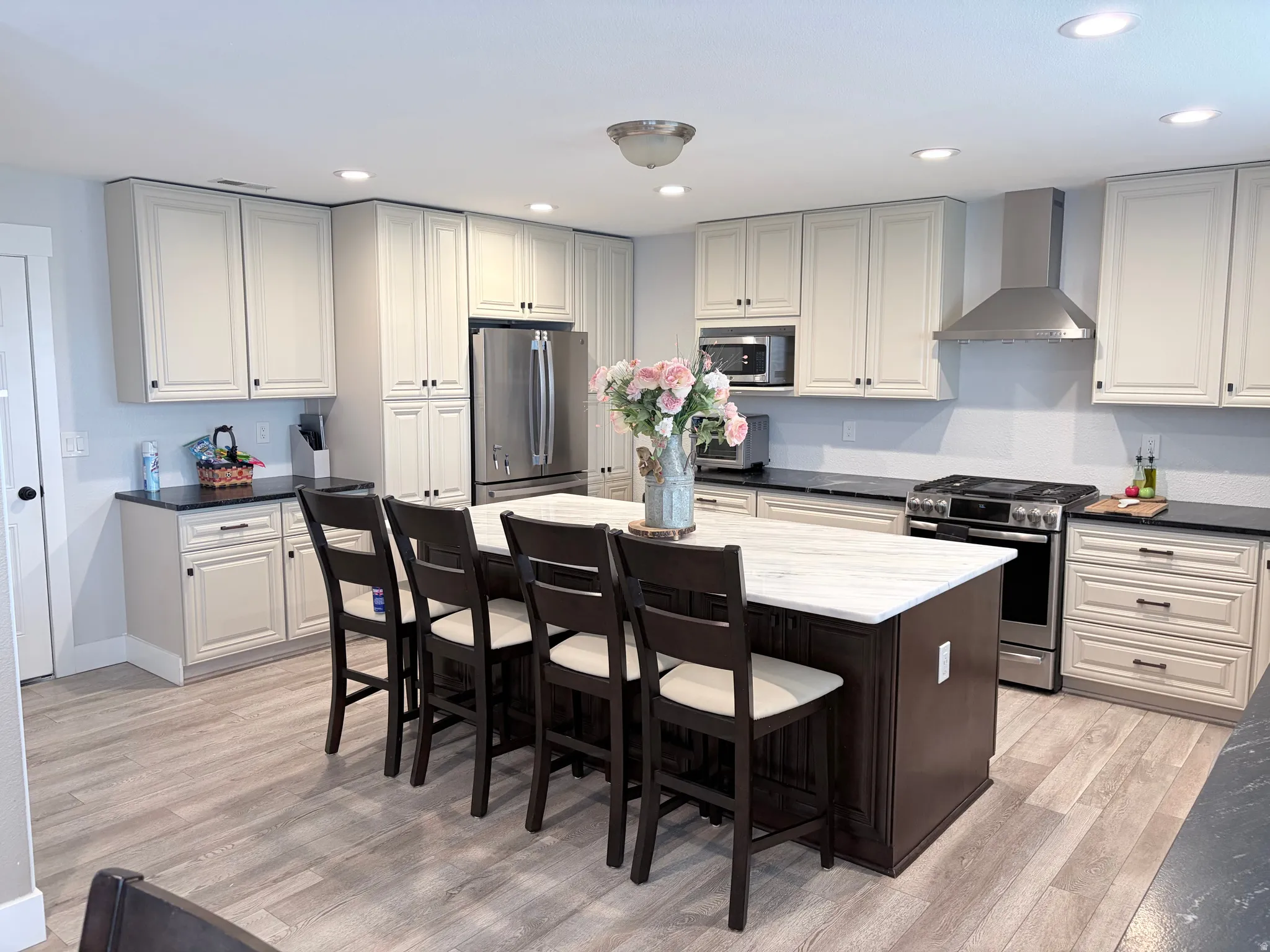 Spacious kitchen featuring a central island with a white countertop, extensive light-toned cabinetry, stainless steel appliances, dark countertops, and wood-finish flooring