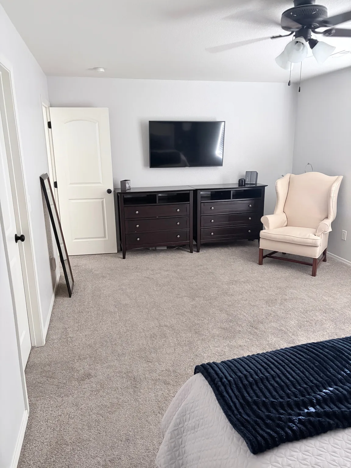 Carpeted room featuring light gray walls, a white paneled door with black hardware, and a ceiling fan with light fixture