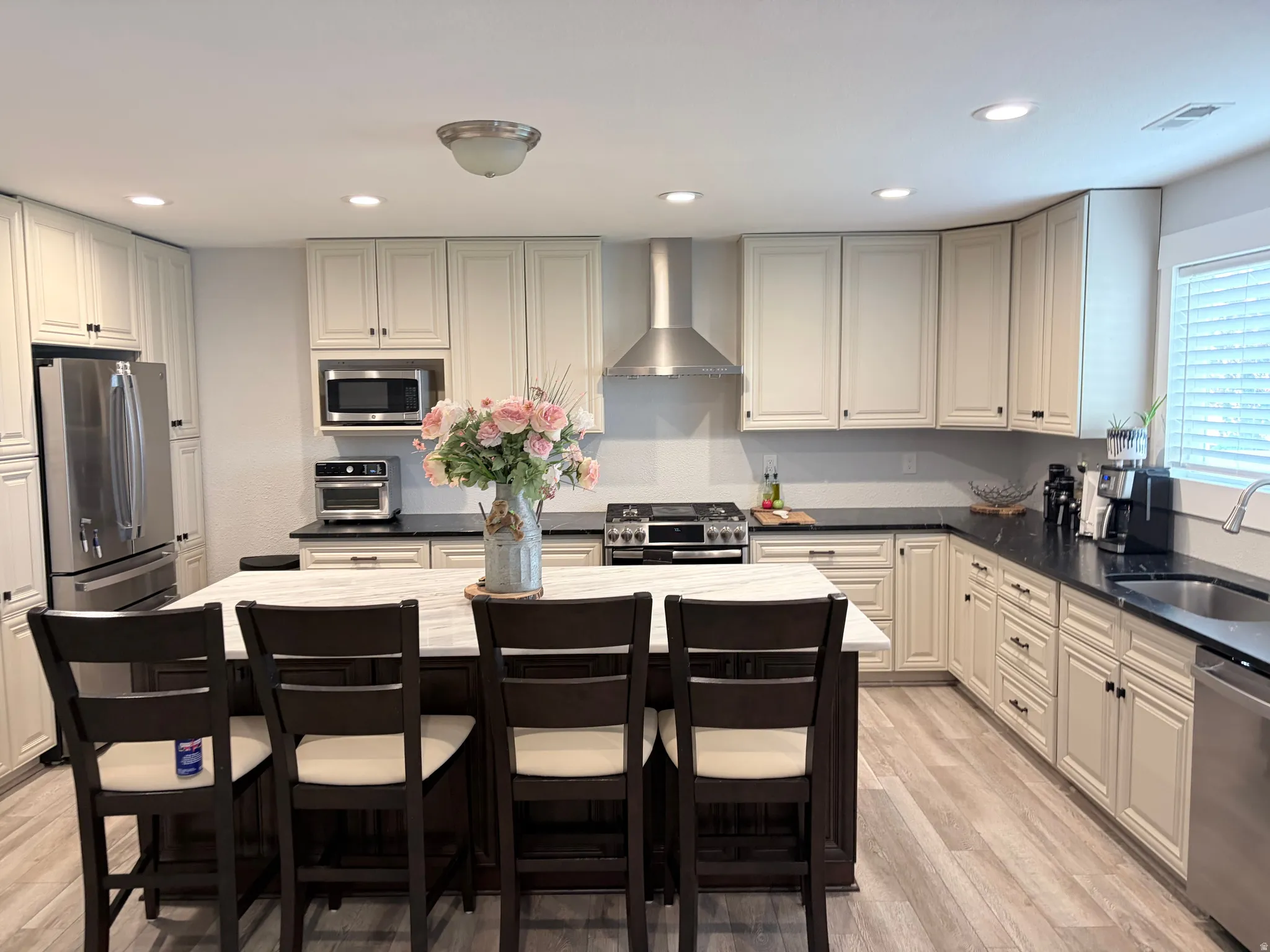 Spacious kitchen featuring an expansive island with a light-toned countertop, ample cream-colored cabinetry, dark countertops, and wood-finish flooring