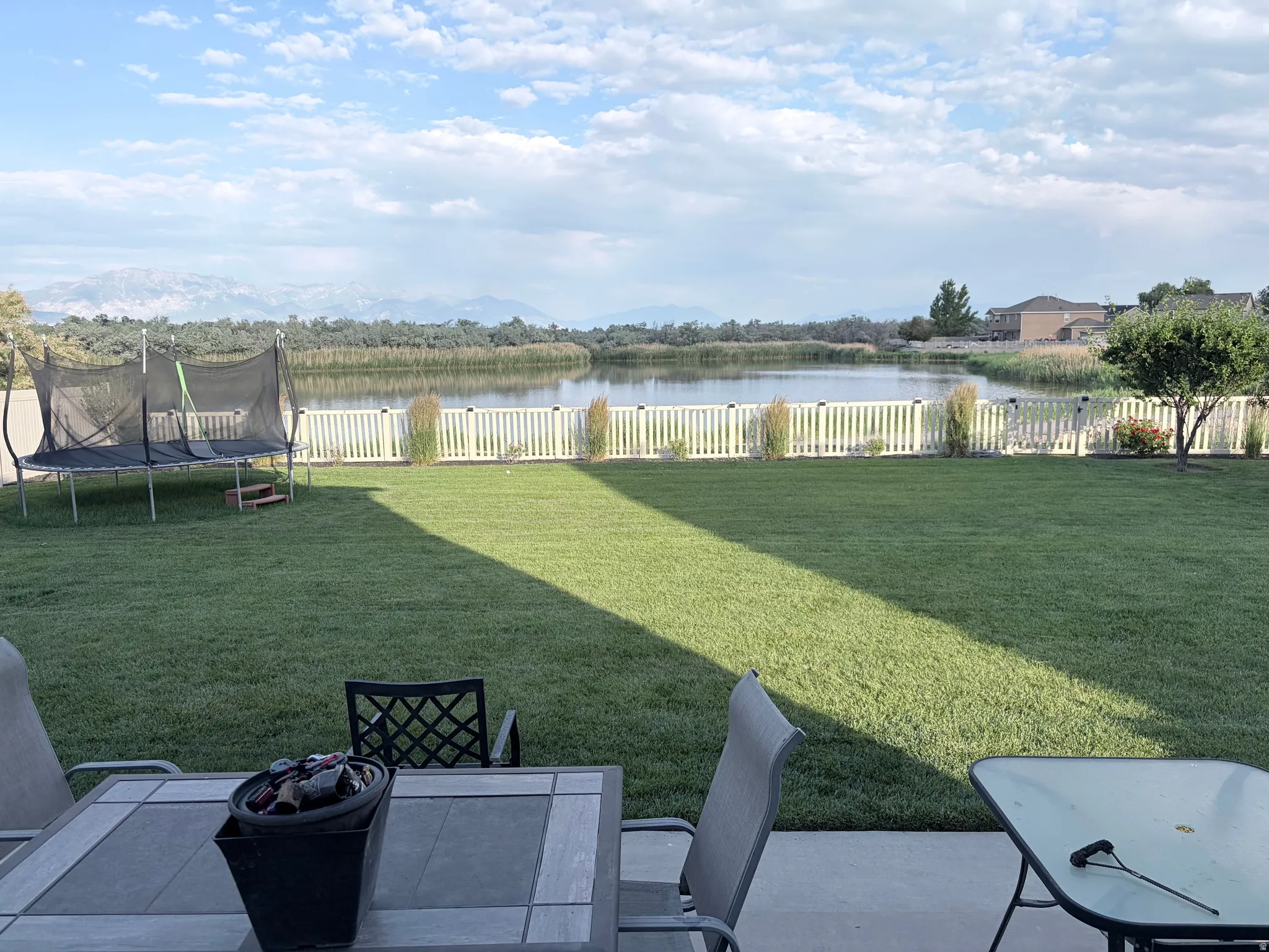 Expansive backyard featuring a manicured lawn, white picket fence, and a calm water feature