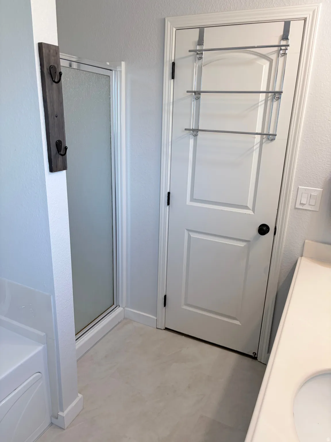 Shower enclosure with clear glass paneling, light-toned tile flooring, and a white interior door