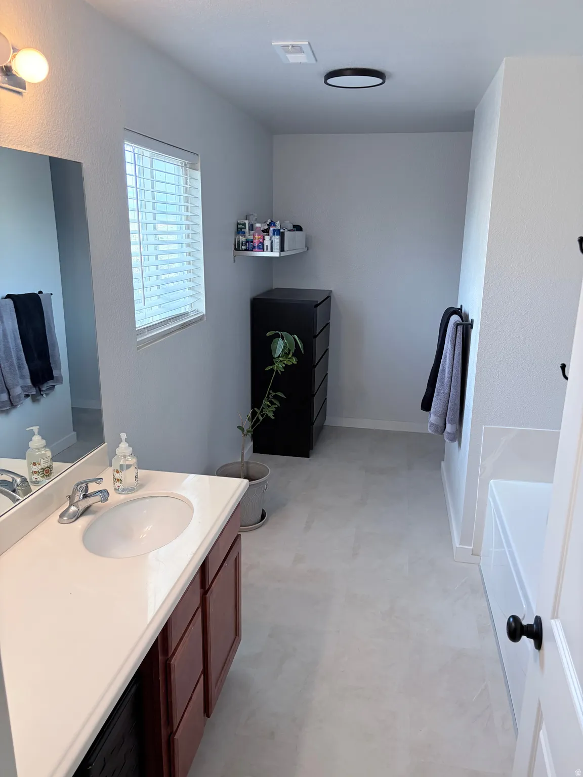 Bathroom featuring a single vanity with a white countertop and wood-finish cabinetry, a window with blinds, and light-toned flooring