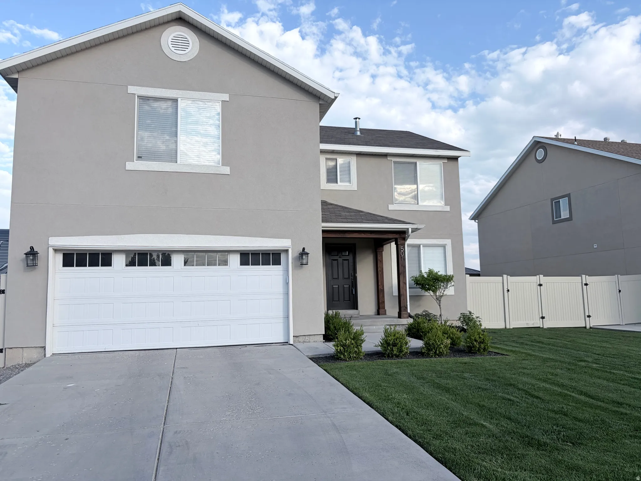 Modern stucco exterior with a two-car garage, covered porch entry, and a manicured lawn