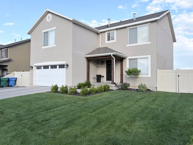 Stucco exterior with a covered entry featuring wooden support columns, a two-car garage, manicured lawn, and perimeter fencing