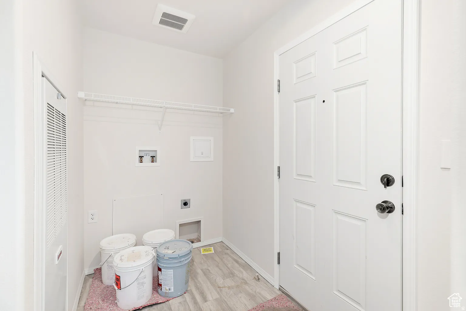Dedicated utility area featuring wood-finish flooring, a six-panel entry door with matte black hardware, and an accessible electrical panel