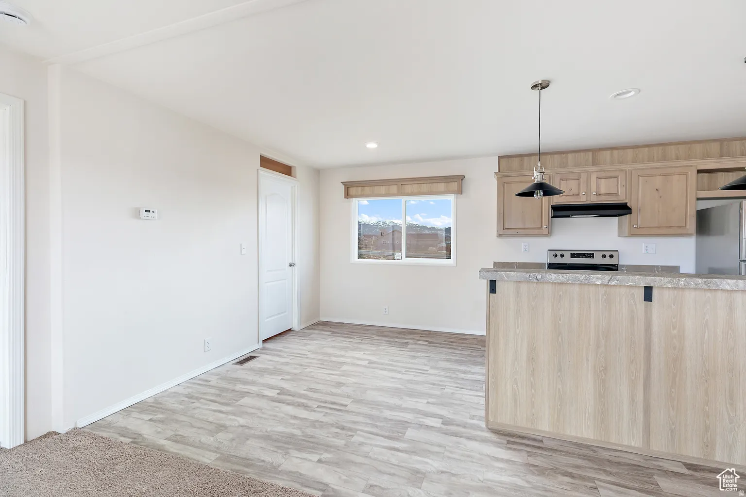 Open-concept kitchen and dining area featuring wood-finish flooring, a kitchen island with stone-look countertop, light-toned cabinetry, stainless steel appliances, and a window with a mountain backdrop