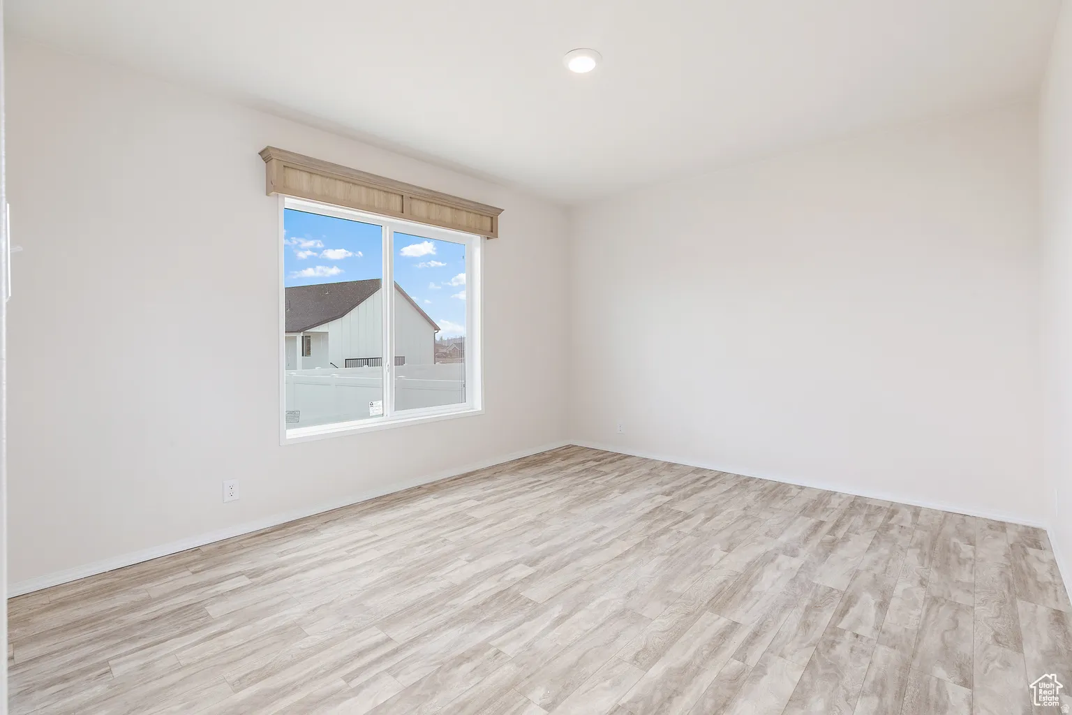 Room featuring light wood-finish flooring, white walls, and a large window with a decorative wood valance