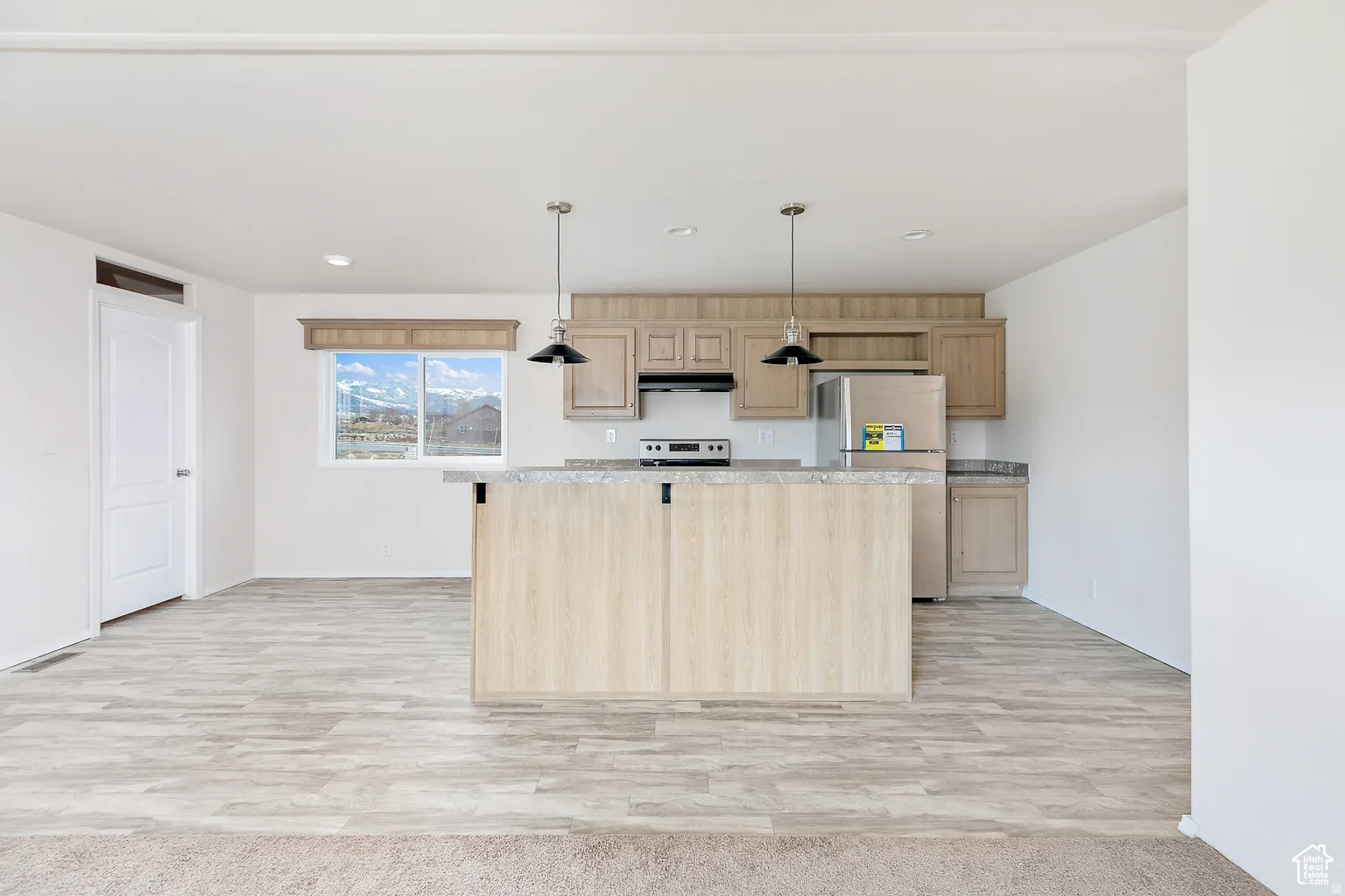 Open-concept kitchen featuring light wood-finish cabinetry, a central island with a stone-finish countertop, and stainless steel appliances