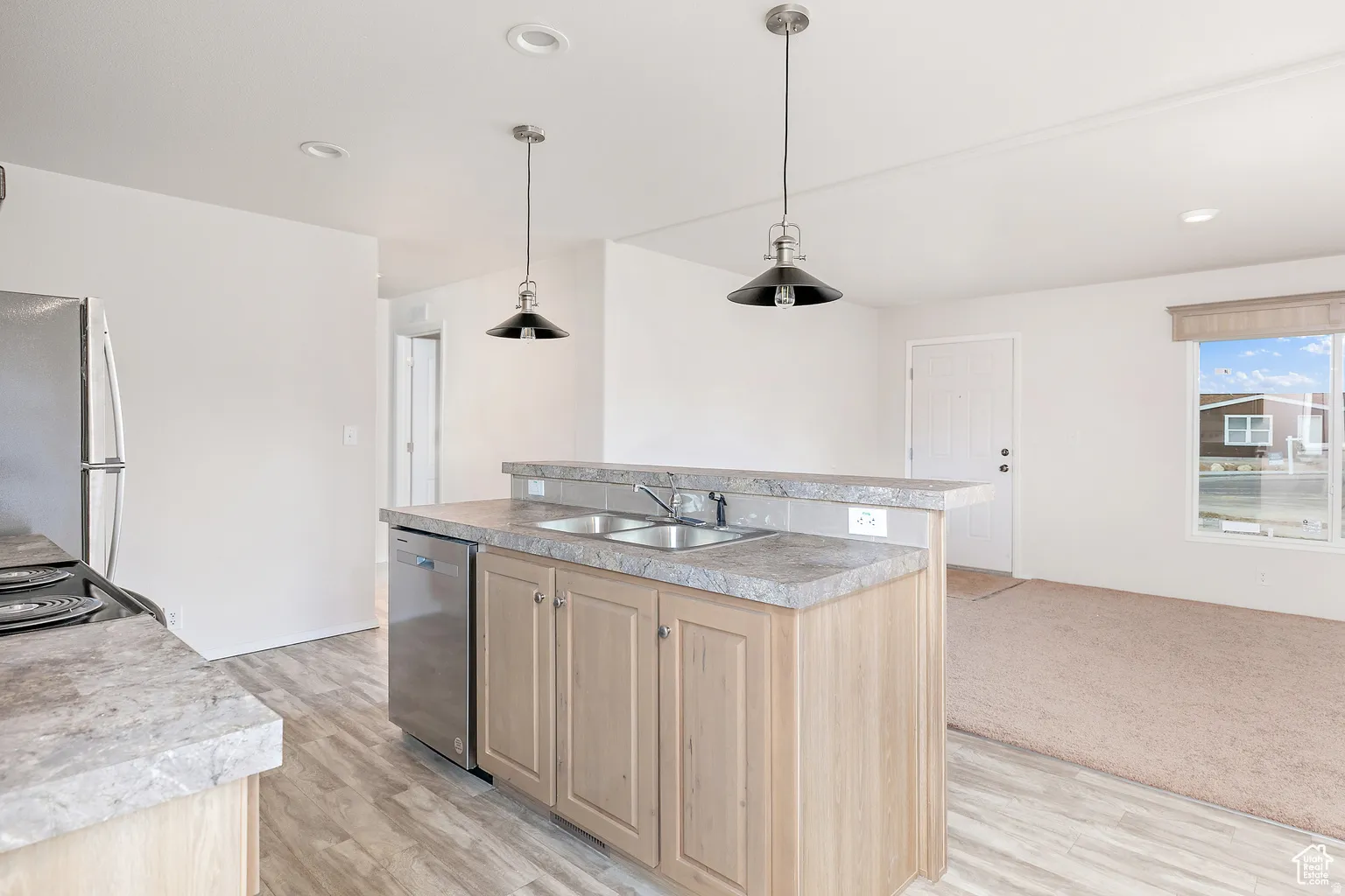 Kitchen island featuring a double-basin sink, light wood-finish cabinetry, and stone-look countertops