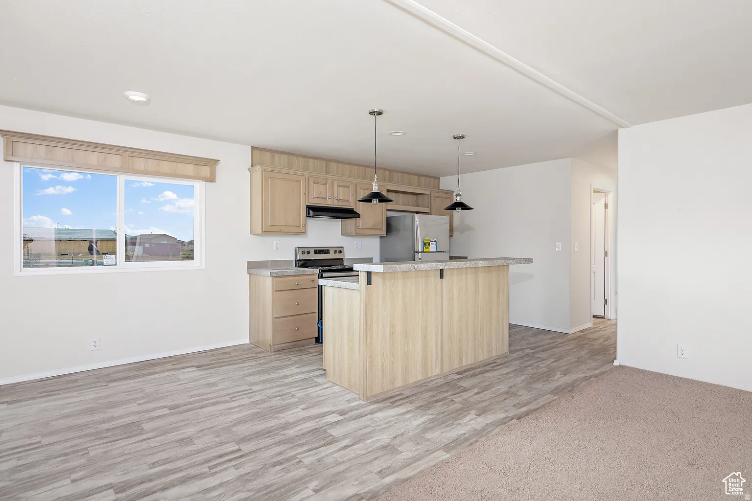 Open-concept living space featuring a kitchen island with seating, pendant lighting, wood-finish flooring, and a large window