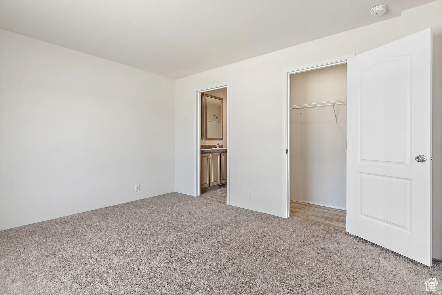 Carpeted room featuring a white wall, a closet with bifold doors, and an entry to a bathroom