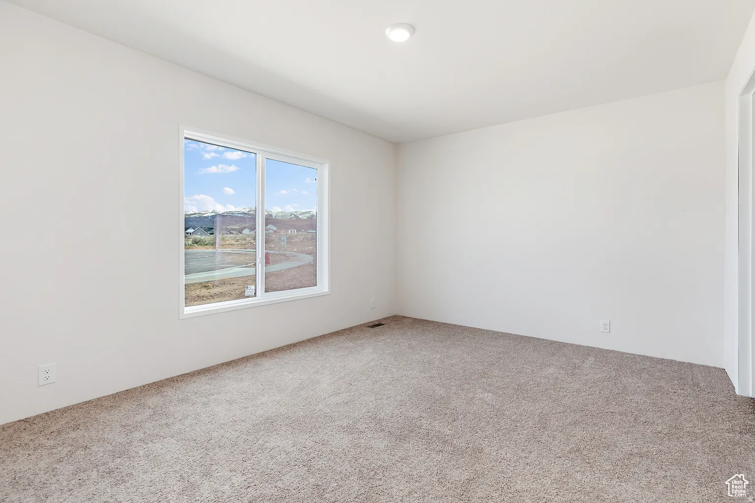 Bright room featuring neutral wall paint, warm-toned carpet, a large window with white trim, and a flush-mount ceiling light