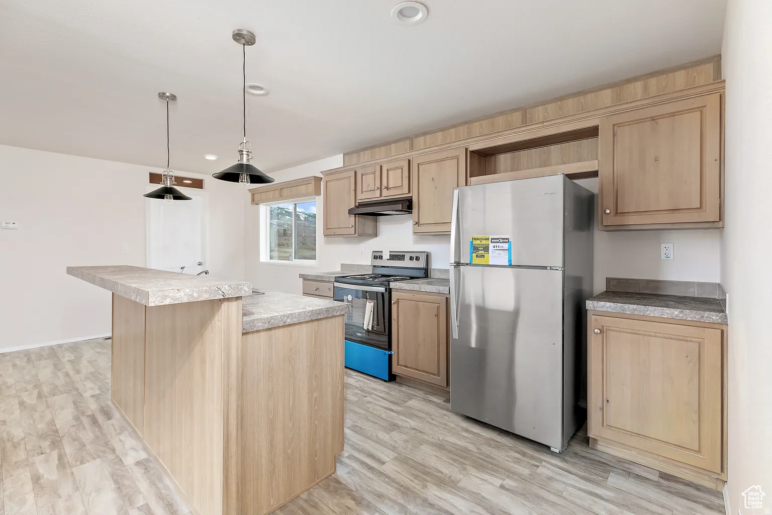 Kitchen featuring a central island with an extended breakfast bar, light wood-finish cabinetry, and stainless steel appliances