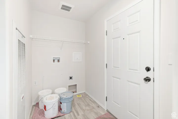 Dedicated utility area featuring wood-finish flooring, a six-panel entry door with matte black hardware, and an accessible electrical panel