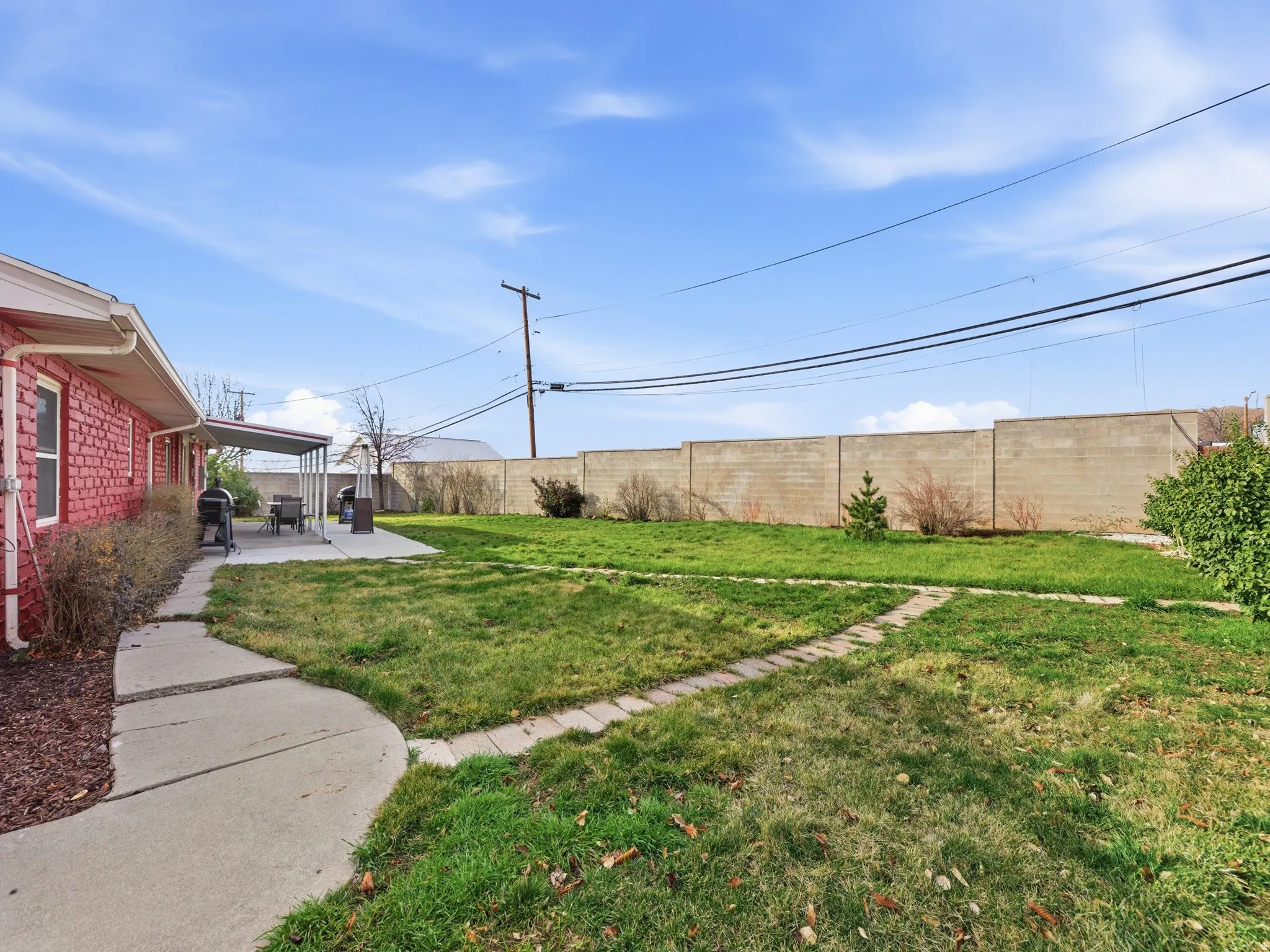Backyard featuring a red brick exterior, concrete patio with awning, expansive lawn, concrete block perimeter wall, and a curved concrete pathway