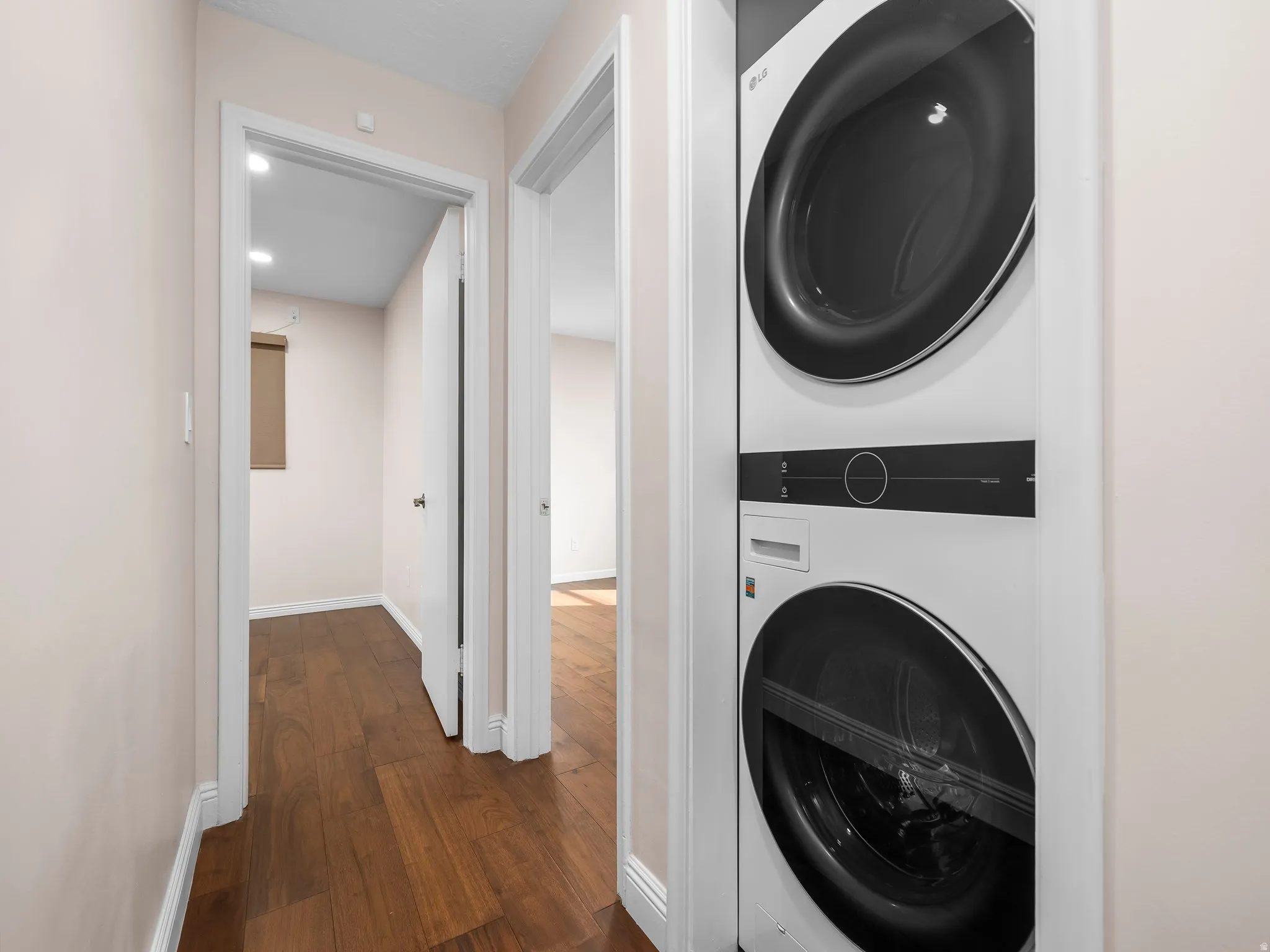 Hallway featuring wood-finish flooring, light-toned walls, white trim, and a built-in stacked washer and dryer unit
