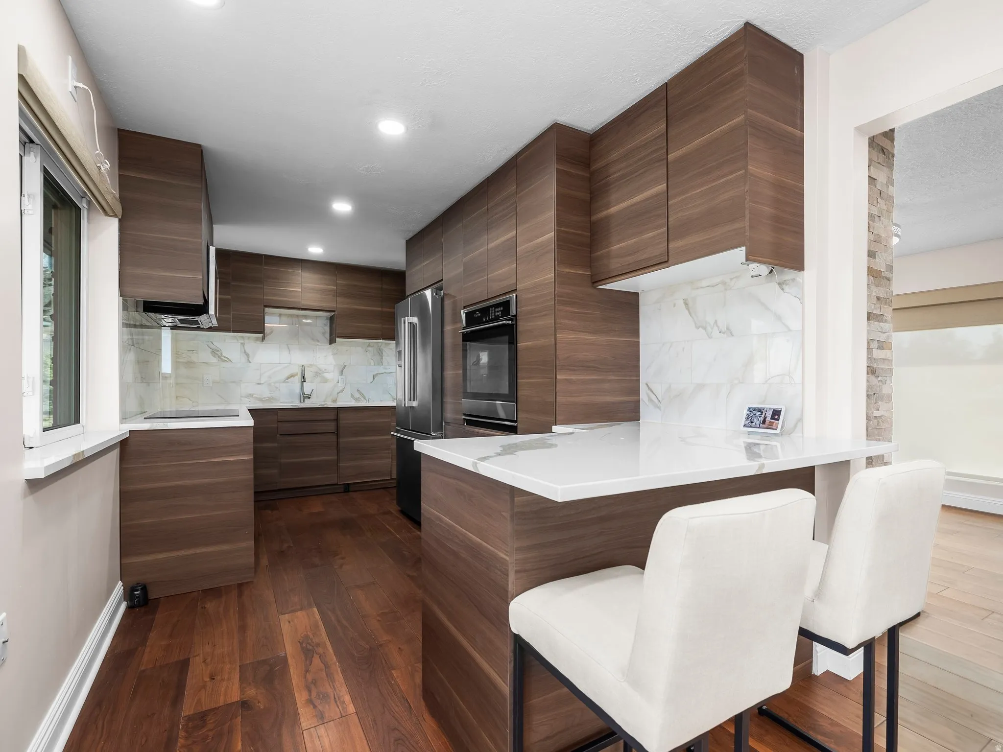 Modern kitchen featuring wood-finish cabinetry, integrated stainless steel appliances, and a marble-patterned backsplash