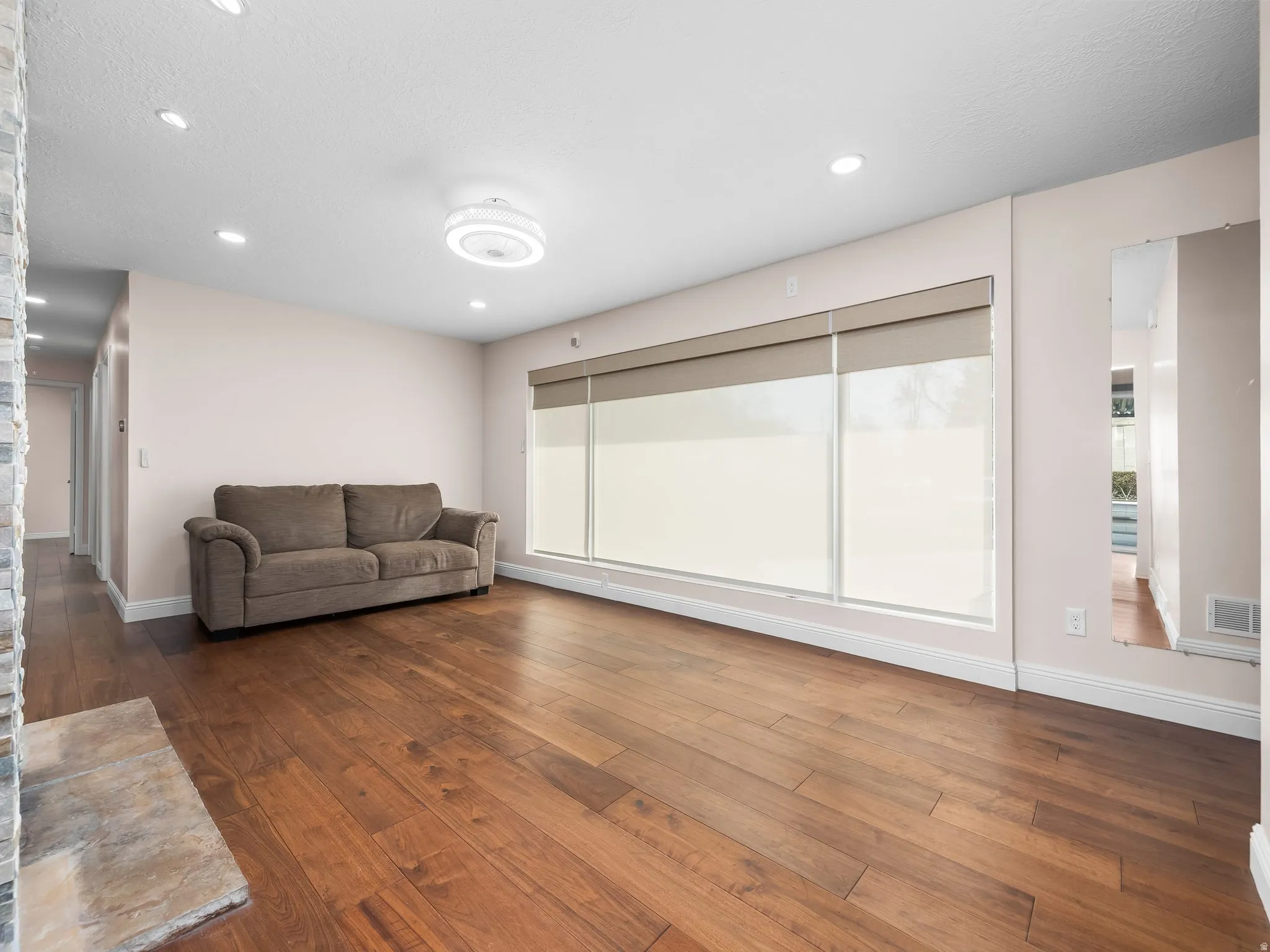 Spacious living area featuring rich wood-finish flooring, recessed lighting, and a modern ceiling light fixture