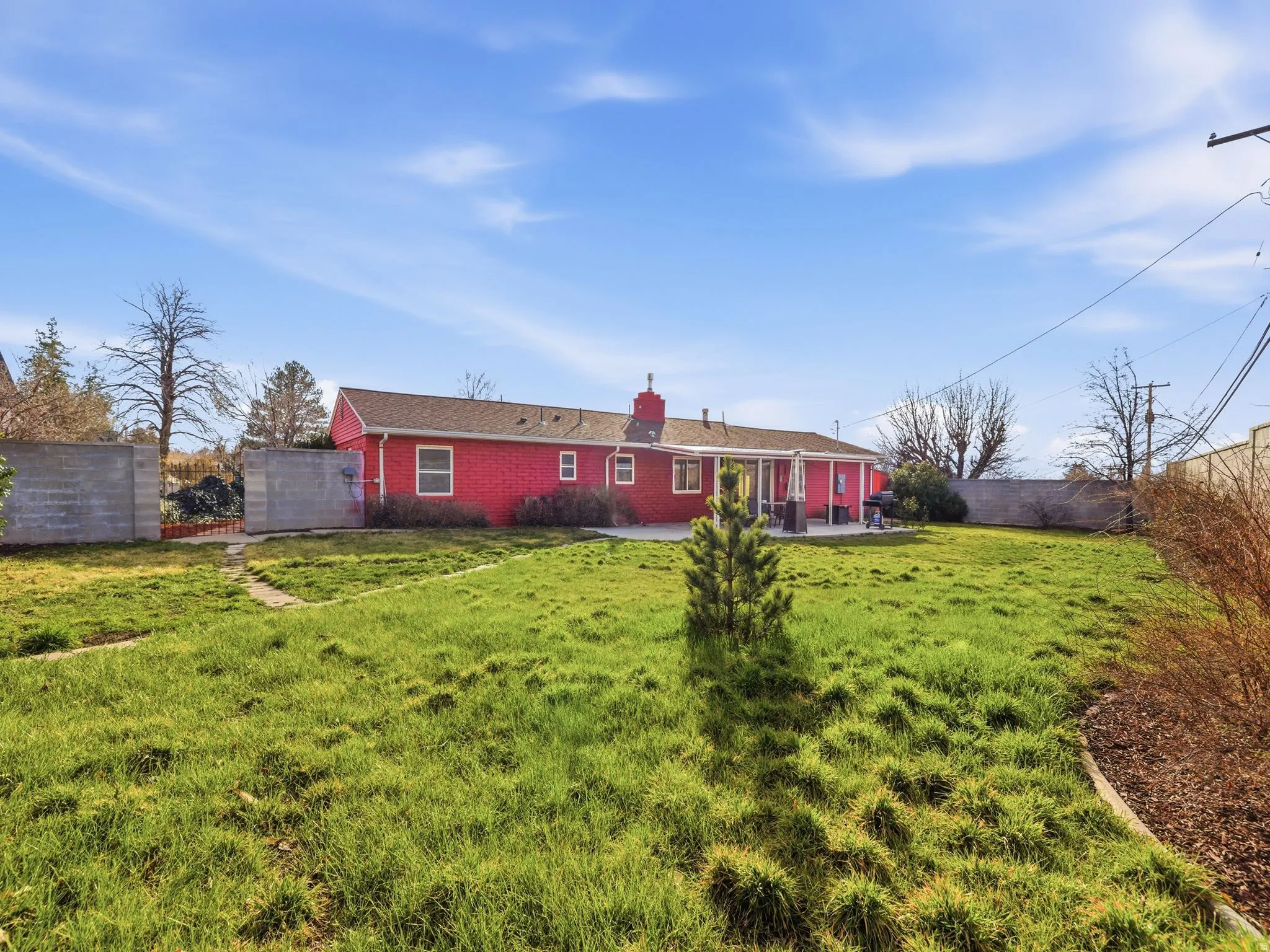 Expansive rear yard featuring a red exterior building with white trim, a concrete patio, and a partial privacy fence