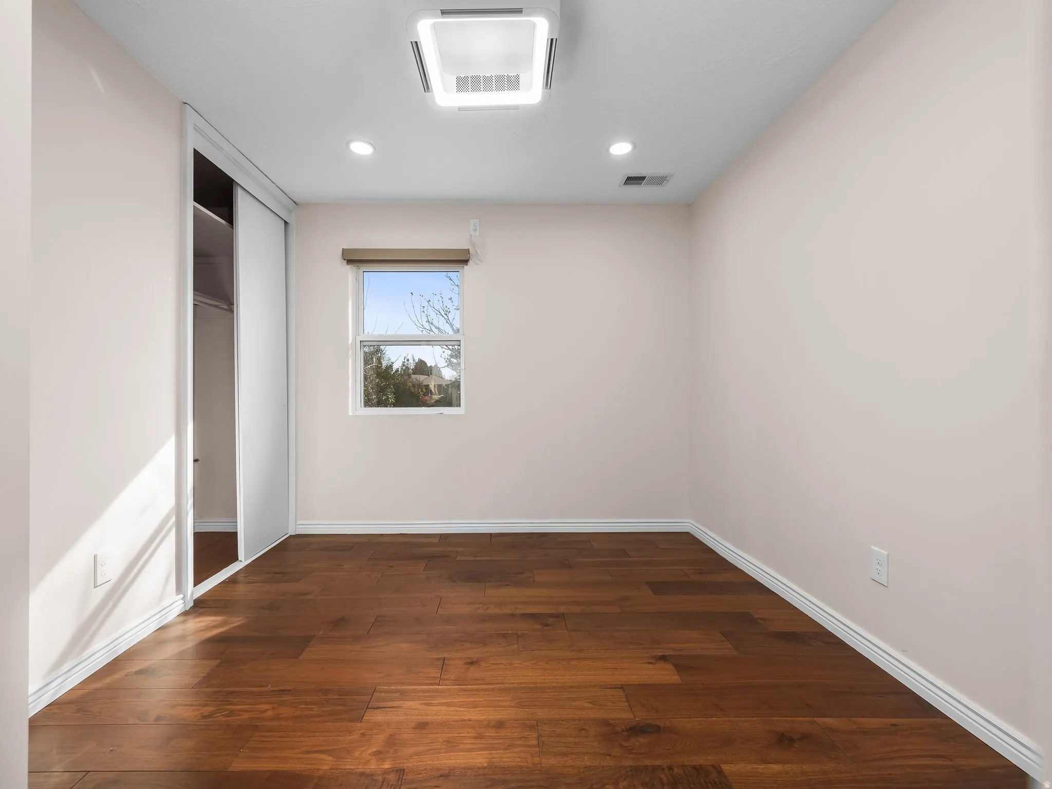 Room featuring wood-finish flooring, recessed lighting, a window with a wood valance, a sliding door closet, and a ceiling-mounted light fixture