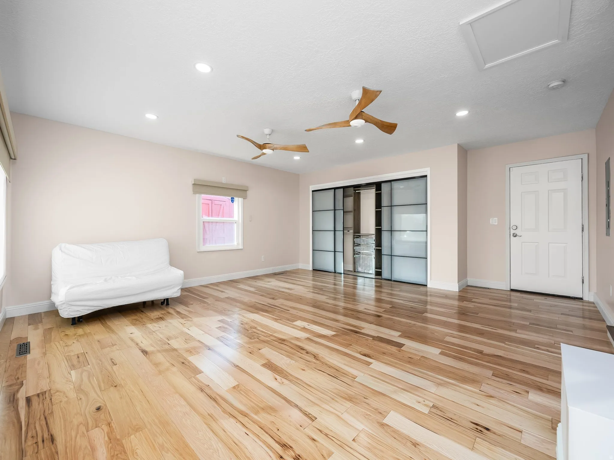 Spacious room featuring light wood-finish flooring, recessed lighting, and two ceiling fans
