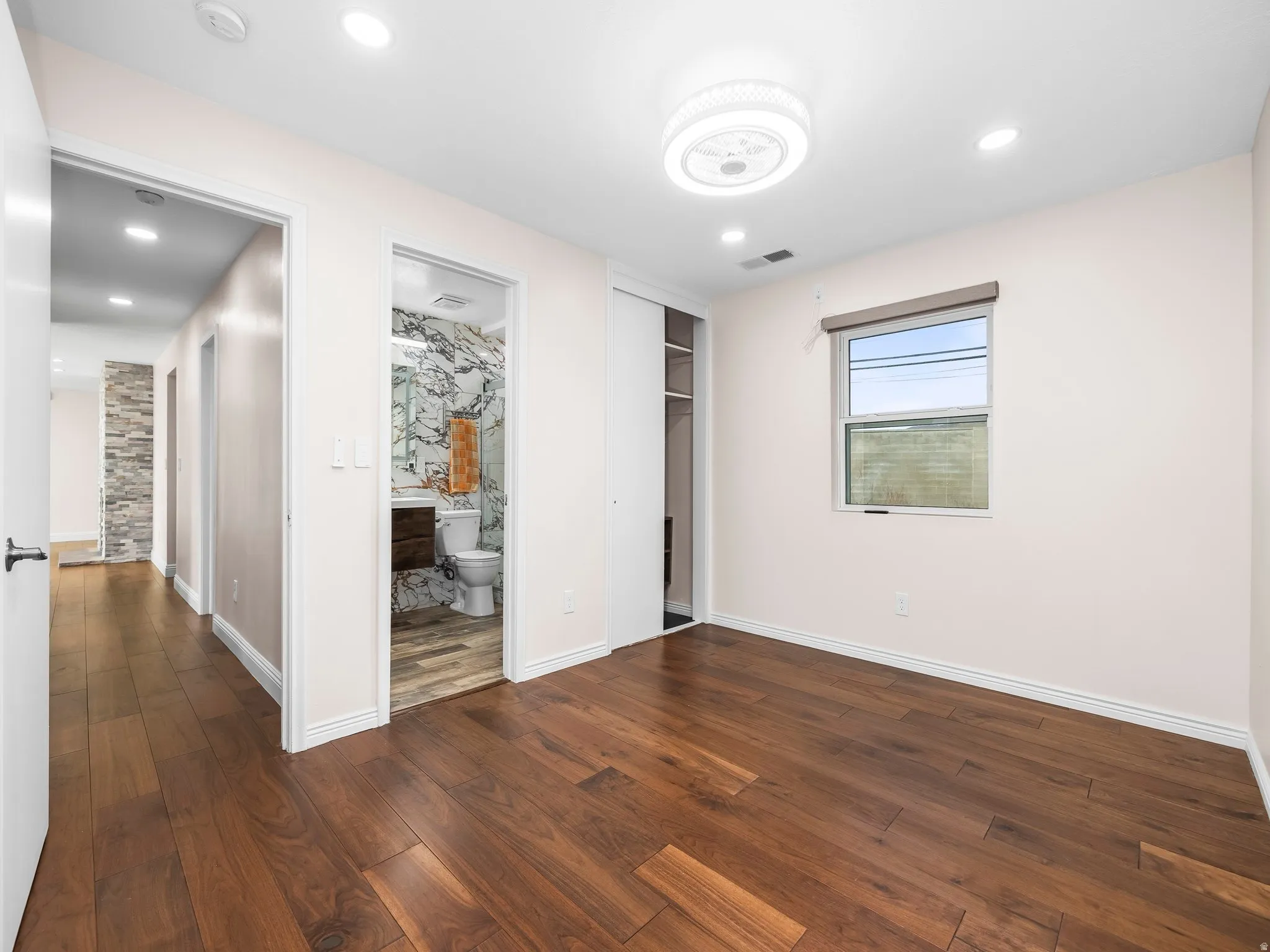 Spacious room featuring wood-finish flooring, a contemporary ceiling light fixture, recessed lighting, and a window with blinds