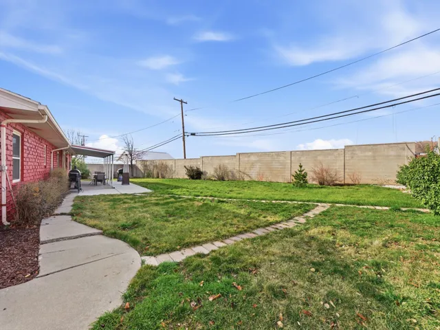 Backyard featuring a red brick exterior, concrete patio with awning, expansive lawn, concrete block perimeter wall, and a curved concrete pathway
