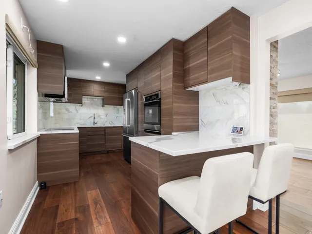 Modern kitchen featuring wood-finish cabinetry, integrated stainless steel appliances, and a marble-patterned backsplash