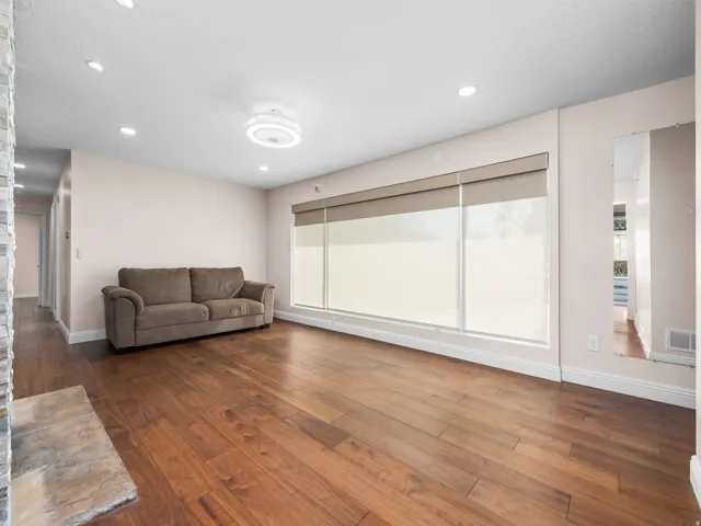 Spacious living area featuring rich wood-finish flooring, recessed lighting, and a modern ceiling light fixture