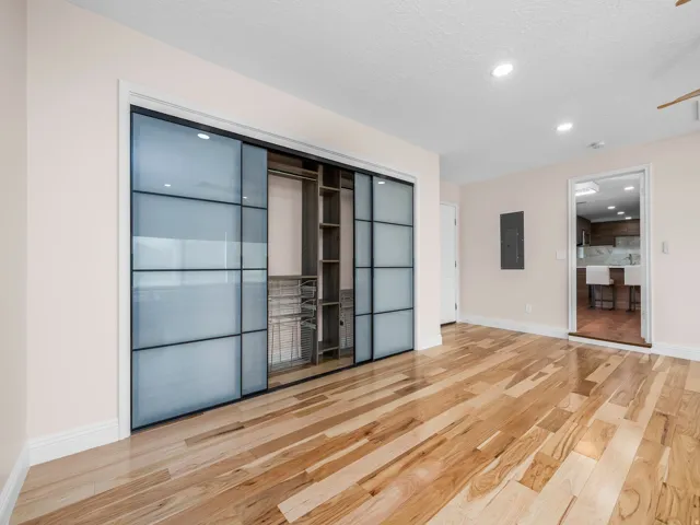 Hardwood flooring throughout featuring a large closet with frosted glass sliding doors and integrated shelving