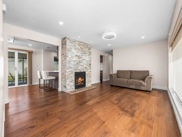 Spacious living area featuring wood-finish flooring, recessed lighting, and a stacked stone fireplace with a raised hearth