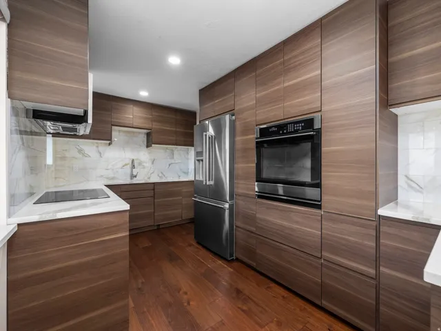 Contemporary kitchen featuring flat-panel wood-finish cabinetry, stainless steel appliances, white countertops, and a full-height tile backsplash