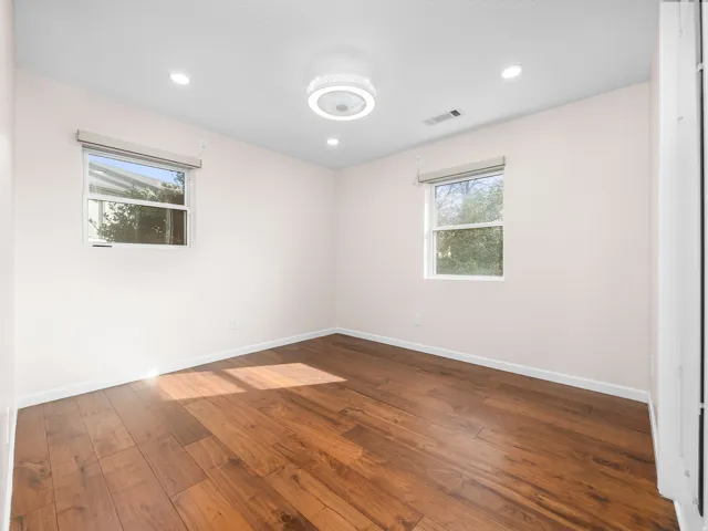 Bright room featuring wood-finish flooring, two windows with roller blinds, recessed lighting, and a modern ceiling fan