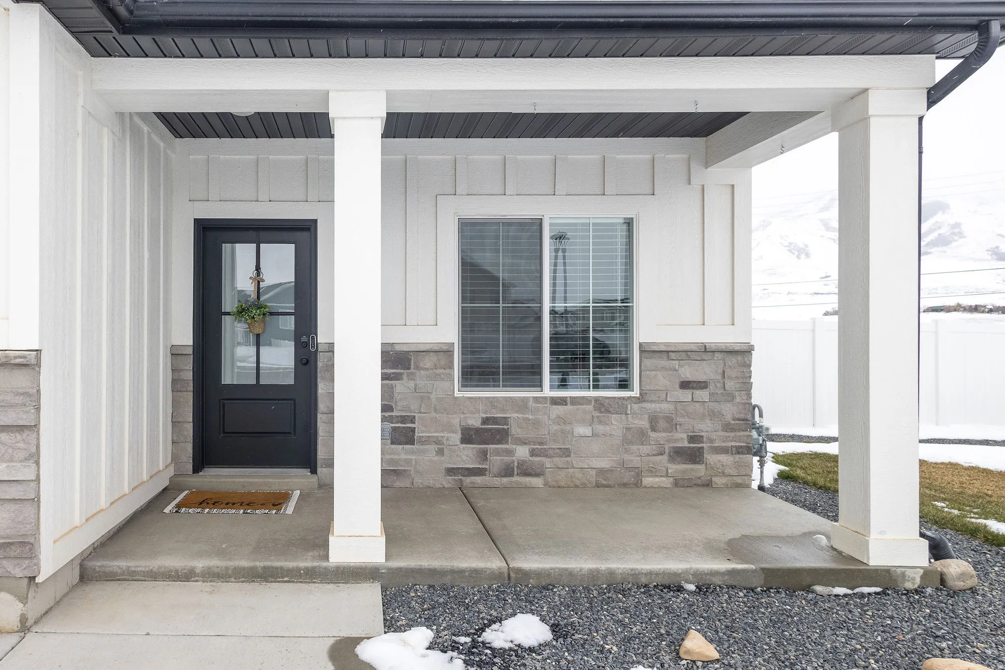 Covered front porch featuring a black paneled door with glass inserts, white board and batten siding, and a stone veneer foundation