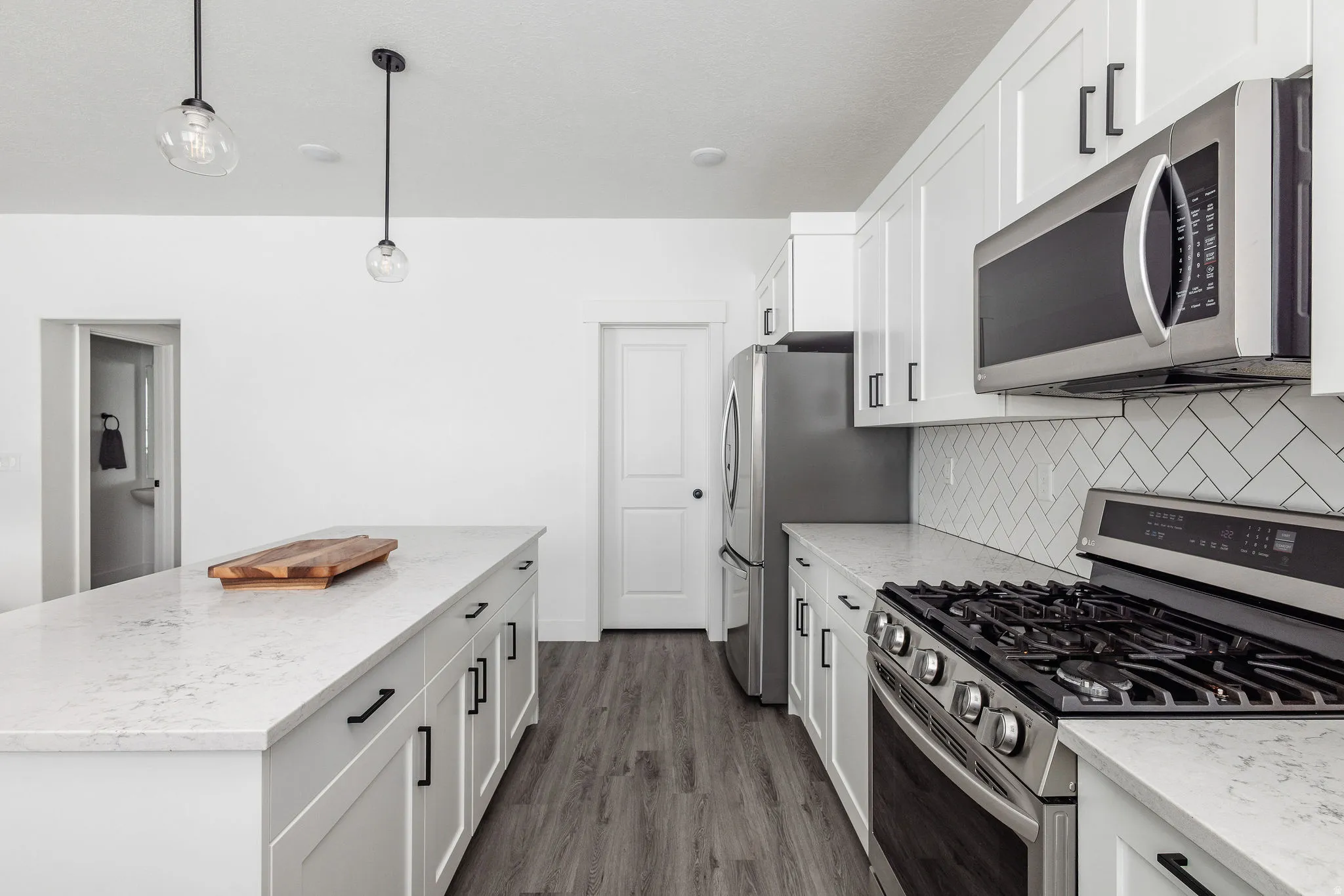 Modern kitchen featuring white cabinetry, quartz countertops, a herringbone tile backsplash, stainless steel appliances, and wood-finish flooring